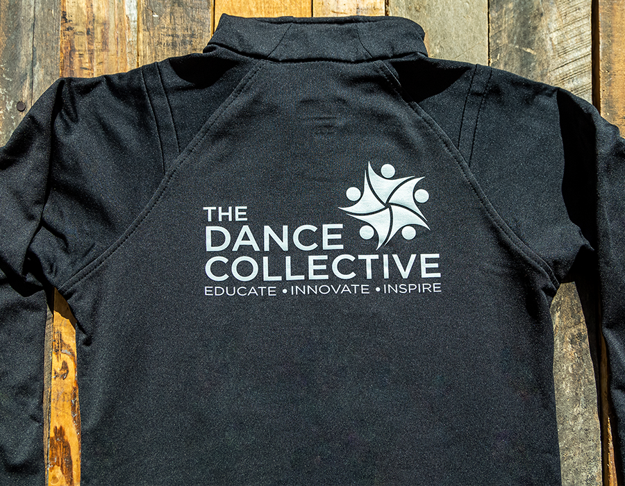 Black performance jacket with The Dance Collective logo printed in white on the back.