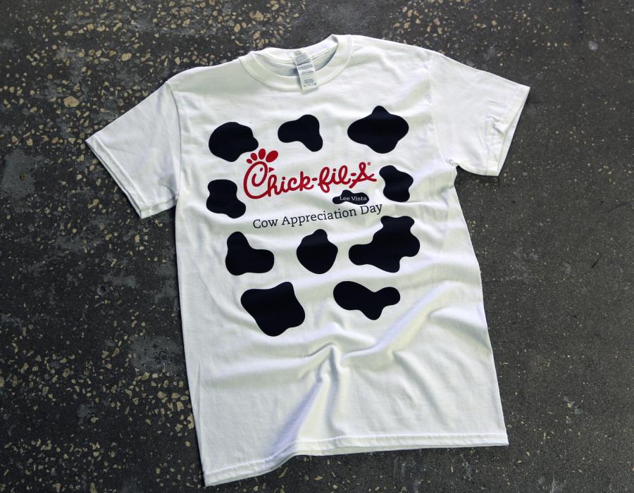 White Gildan T-shirt with Chick-fil-A logo and black cow-print spots laid flat on concrete.