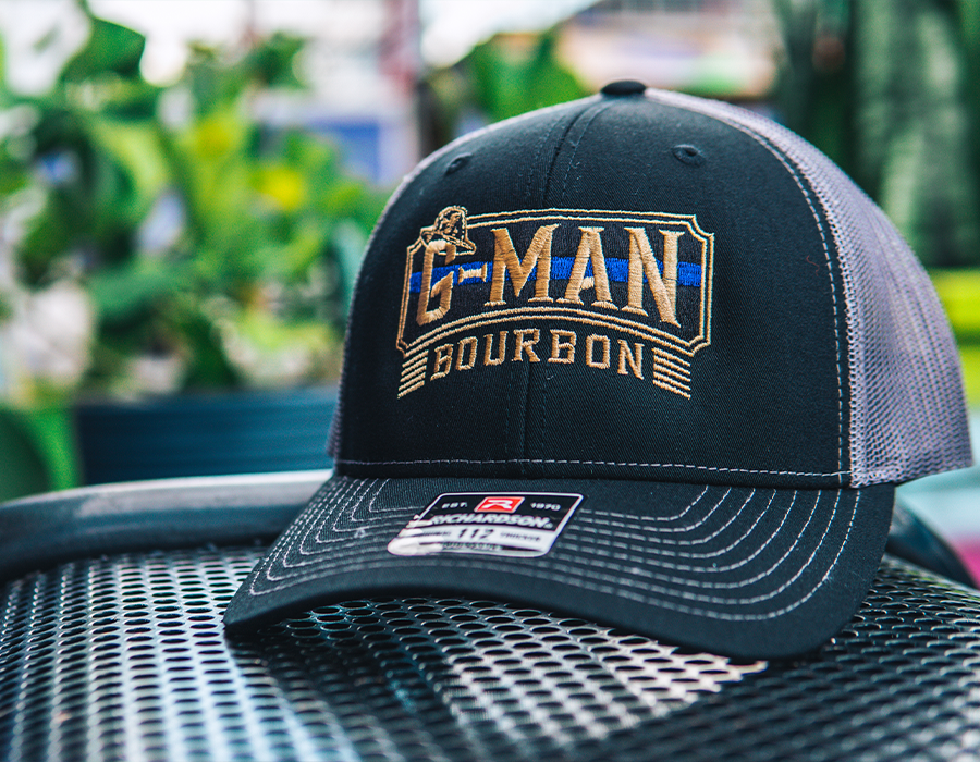 Custom G-Man Bourbon trucker hat with detailed gold, white and blue logo embroidery on the front and mesh back panels.