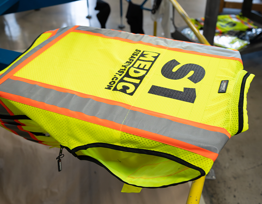 Fluorescent yellow custom safety vest with black screen printed company logo and S1 employee identification in an Orlando screen printing shop.