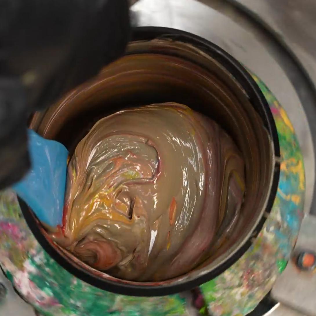 Close-up of upcycling mixed metallic screen printing ink in a bucket, showing swirls of gold, copper, and bronze pigments being stirred for upcycled apparel printing.